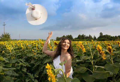 Smiling young woman throwing hat mid air at field