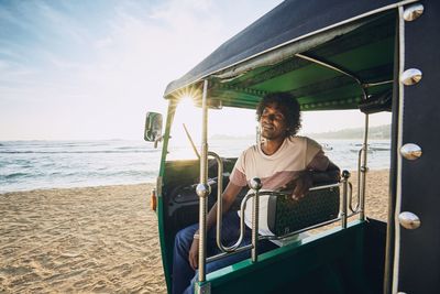 Man sitting at beach against sky