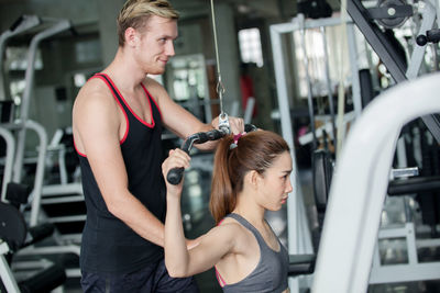 Trainer assisting woman in exercising at gym