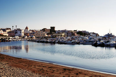 Sailboats in sea by city against clear sky