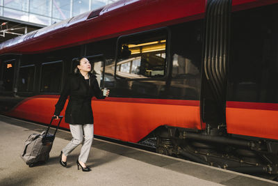 Businesswoman with luggage holding drink while running by train at railroad station