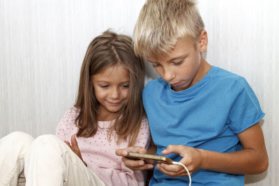Kids playing with mobile phone while sitting in bedroom