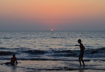 Friends standing on beach against sky during sunset