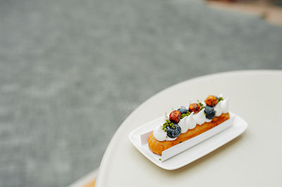 Delicious eclair with white cream, fresh blueberries and caramel on the table of an outdoor cafe.