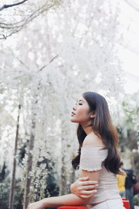 Side view of thoughtful young woman standing against plants in park