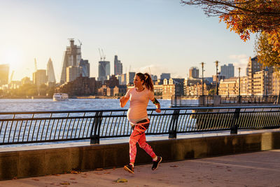 Pregnant woman running on promenade in city during sunset