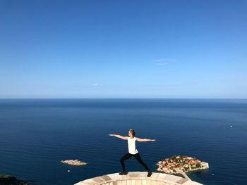 Woman standing by sea against blue sky