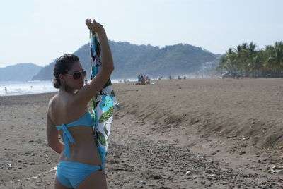 Portrait of young woman standing on beach against sky