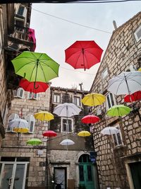 Low angle view of multi colored umbrellas hanging amidst buildings in city