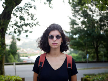 Portrait of young woman wearing sunglasses standing against trees