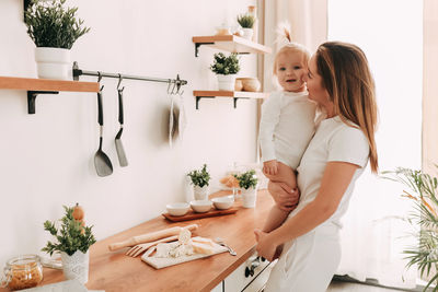 A young mother and a small child prepare lunch together in the cozy bright kitchen of indoors