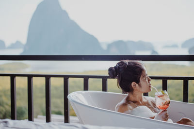 Woman having drink while relaxing in bathtub