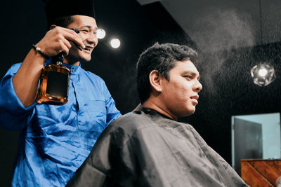Smiling hairdresser spraying water on man head