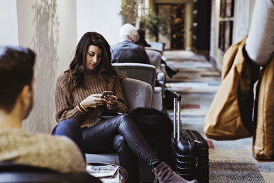 Mid adult woman using mobile phone while sitting in front of boyfriend at hotel