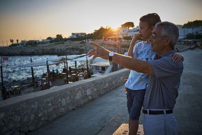 Italy, santa caterina, grandfather and grandson looking at view by sunset