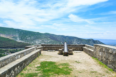 Cannon in castle by mountains against cloudy sky