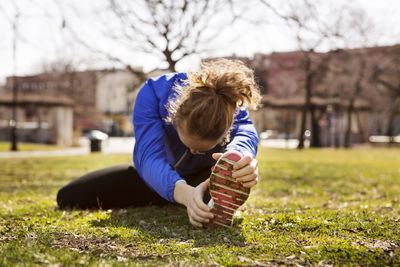 Woman exercising while sitting on field in park