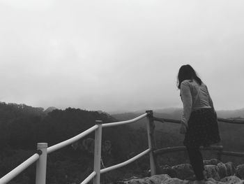 Side view of woman standing on railing against sky