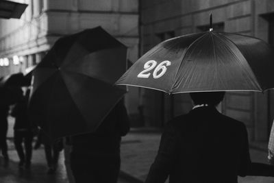 Rear view of man holding umbrella with number in city during monsoon