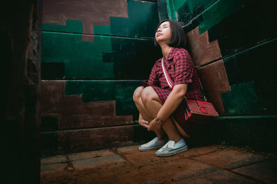 Full length of young woman sitting by wall in room