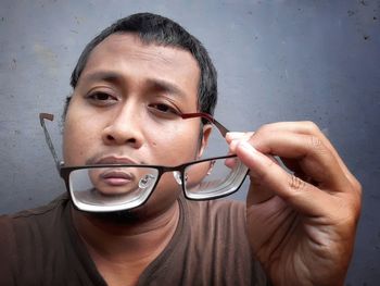 Close-up portrait of man holding eyeglasses against wall