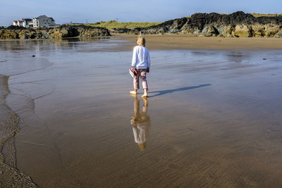 A blond woman walking alone and barefoot in the surf on a sunny day at rhosneigr beach, anglesey, uk