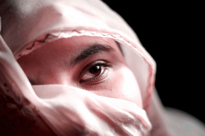 Close-up of woman face covered with scarf against black background