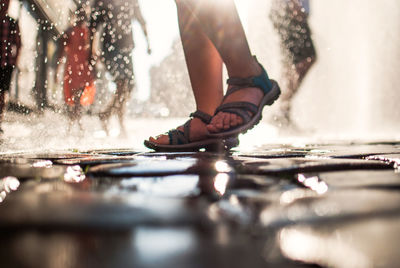 Low section of person walking on wet street during sunny day