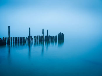 Wooden posts in sea against clear sky