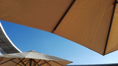 Low angle view of umbrellas against clear blue sky