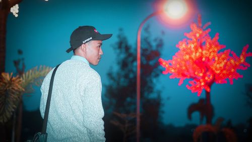 Side view of young man standing against illuminated wall