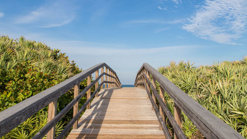 Boardwalk leading towards wooden footbridge against sky