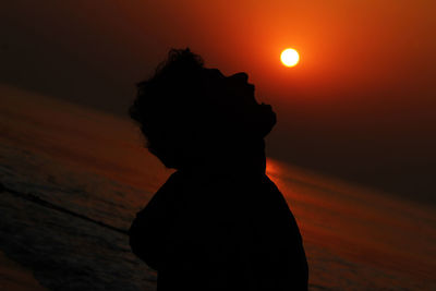 Silhouette woman standing against orange sunset sky