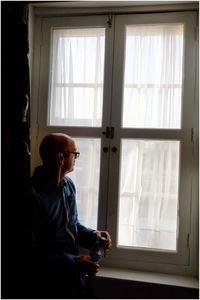 Side view of young man looking through window at home
