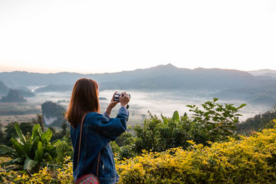 Rear view of woman photographing against mountain range