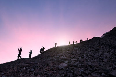 Silhouette people on rock against sky during sunset