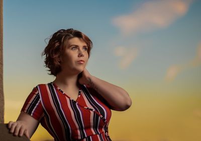 Portrait of young woman looking away against sky during sunset