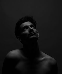 Shirtless mature man looking up against black background