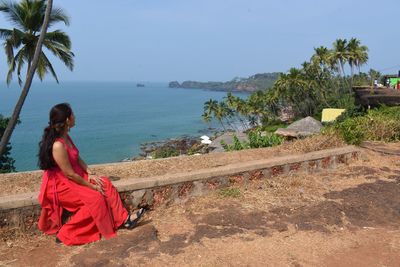 Young woman sitting on palm tree by sea against sky