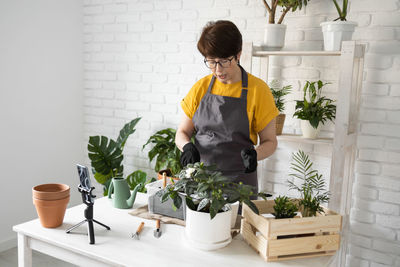 Rear view of woman holding potted plant on table at home