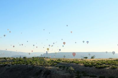 Hot air balloons flying over land against clear blue sky