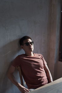 Young man wearing sunglasses sitting against wall