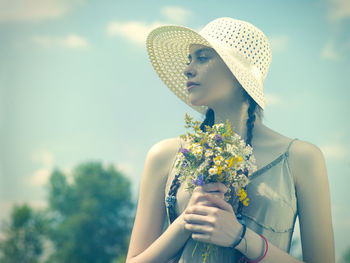 Midsection of woman holding flowering plant against blurred background