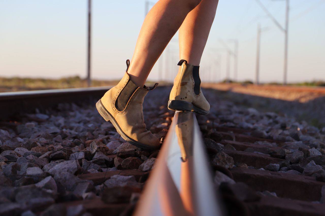 human leg, low section, track, railroad track, rail transportation, one person, real people, shoe, human body part, nature, body part, transportation, sky, selective focus, leisure activity, day, lifestyles, solid, standing, outdoors, surface level, pebble, human limb, gravel, human foot, jeans