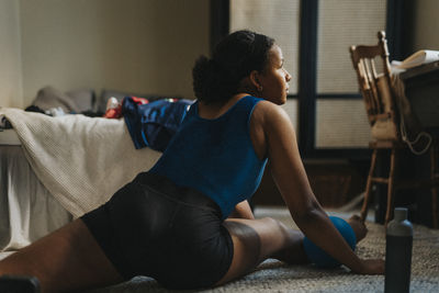 Female athlete practicing exercise while sitting on carpet in bedroom