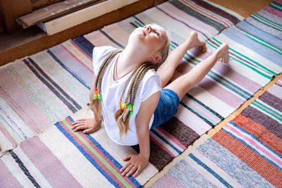 Caucasian girl with braids in a white t-shirt is doing yoga, stretching at home on a striped rag