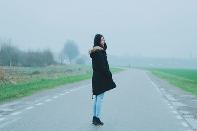 Woman standing on road against sky in foggy weather