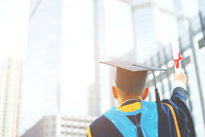 Rear view of woman wearing graduation gown standing in city