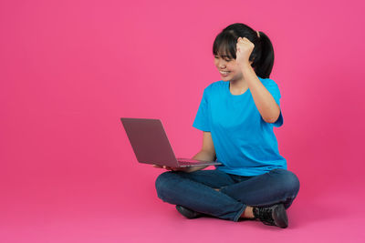 Full length of happy girl sitting on pink background