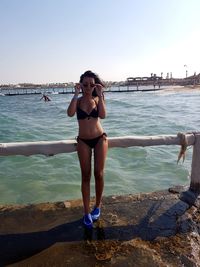 Full length of young woman standing in sea against sky